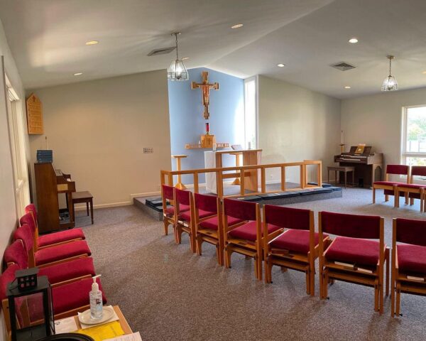 Interior view of a small chapel with a crucifix and red-cushioned chairs.
